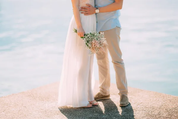Brudgummen omfamnar bruden på stranden. Bröllop i Montenegro — Stockfoto