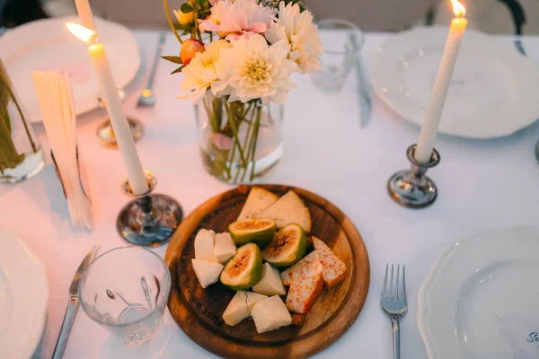 Queso rebanado e higos en un plato de madera sobre una mesa con velas — Foto de Stock