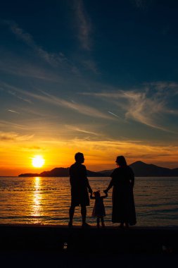Batan güneşin ve denizin zemin karşı çocuklu bir aile silüeti