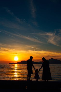 Batan güneşin ve denizin zemin karşı çocuklu bir aile silüeti