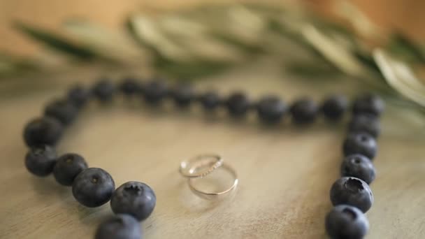 Wedding rings in a heart of a blueberry on a table, next to a br — Stock Video