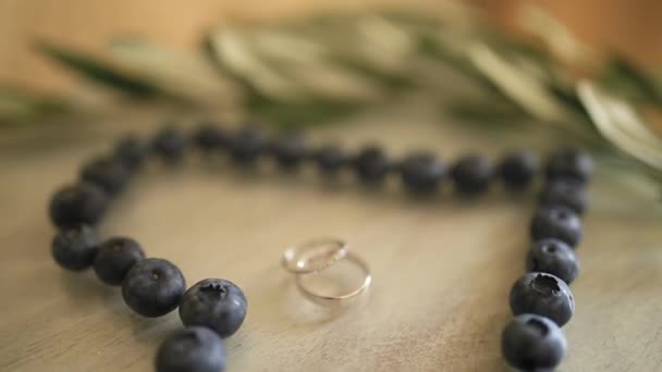 Wedding rings in a heart of a blueberry on a table, next to a br — Stock Video