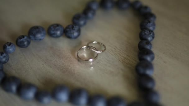 Anillos de boda en un corazón de un arándano en una mesa, al lado de un br — Vídeo de stock