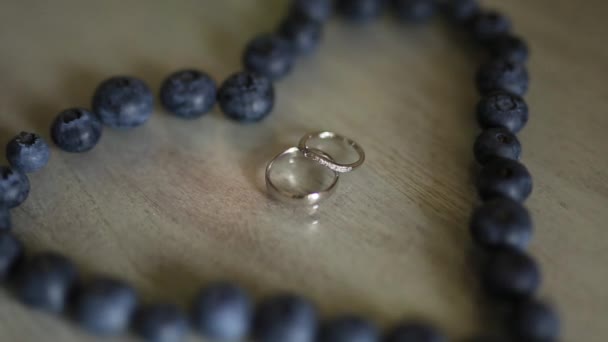 Wedding rings in a heart of a blueberry on a table, next to a br — Stock Video