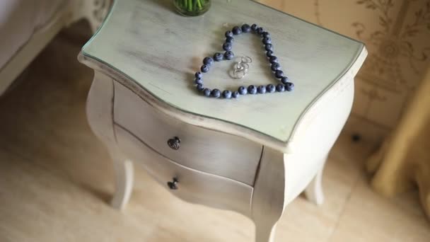 Весільні кільця в серці чорниці на столі, поруч з бром — стокове відео
