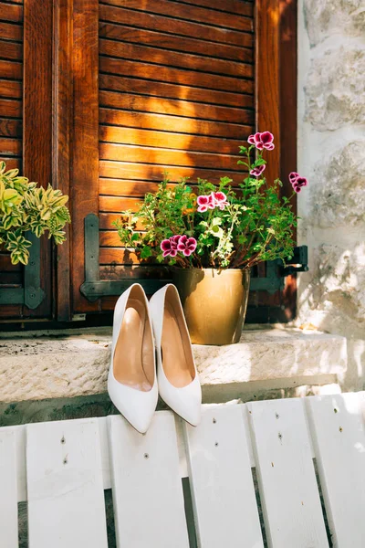Zapatos de novia blancos en un banco blanco y flores en el backgrou —  Fotos de Stock