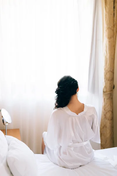 Una chica con una bata de seda está sentada en la cama y mirando —  Fotos de Stock