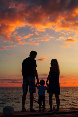 Denizde bir çocukla ebeveyn silüeti. Aile sahilde ben