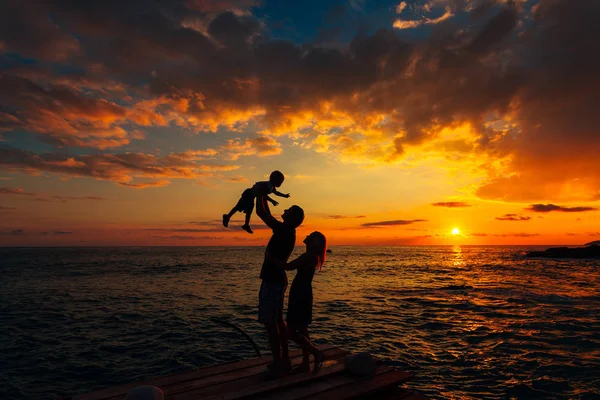 Denizde bir çocukla ebeveyn silüeti. Aile sahilde ben