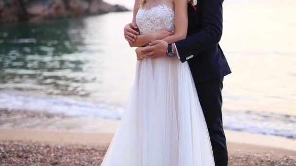 Brudgummen omfamnar bruden på stranden. Bröllop i Montenegro — Stockvideo