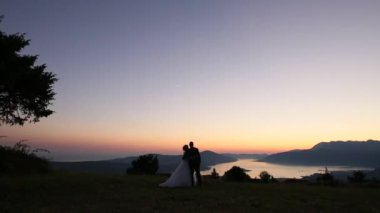 Bir yeni evli çift gün batımında dağlarda silüeti. Düğünü