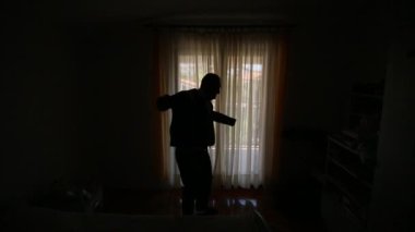 Bir adam onun j giyinme bir pencere arka planda silüeti