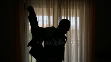 Bir adam onun j giyinme bir pencere arka planda silüeti
