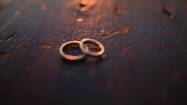 Свадебные кольца на темной деревянной текстуре на закате — стоковое видео
