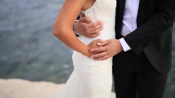 Brudgummen omfamnar bruden på stranden. Bröllop i Montenegro — Stockvideo