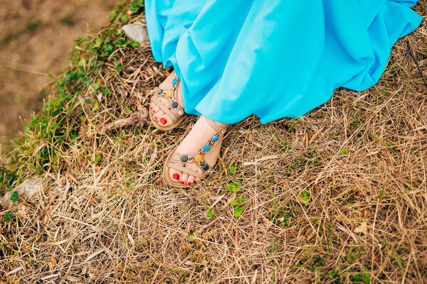 Female feet in sandals. On dry grass. A girl in a blue sarafan.