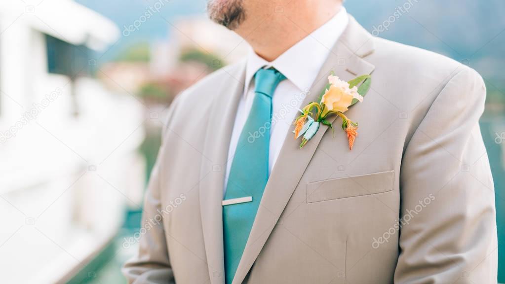 The groom with a beard boutonniere on the lapel of a light jacke