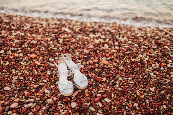 Zapatos de boda de la novia en la orilla del mar, en el guijarro del mar —  Fotos de Stock