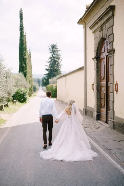 Pengantin wanita dan pengantin pria yang cantik berjalan bergandengan tangan jauh dari kamera di luar Vila Medici di Lilliano Wine Estate, Toscana, Italia. — Stok Foto