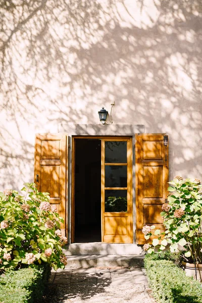 Old wooden door open and the facade of the Medici Villa of Lilliano Wine Estate, Tuscany, Italy under the shade of trees.