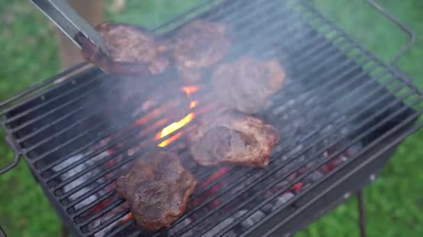 Pečené steaky na grilu nad otevřeným ohněm. Šéfkuchař obrací steaky kleštěma.. — Stock video