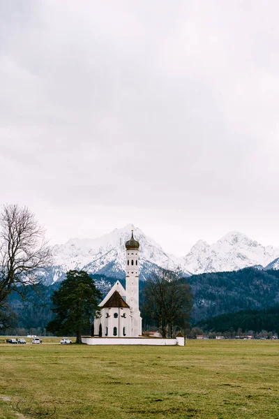 Szent Kolomán templom Németországban, Bajorországban, a Neuschwanstein kastély közelében, kilátással a hófödte hegyekre márciusban — Stock Fotó