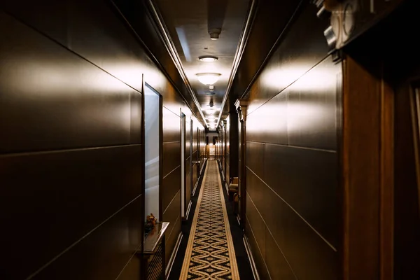 Dark hotel corridor. A long carpet with a pattern, wooden wall cladding. Deserted hotel corridor