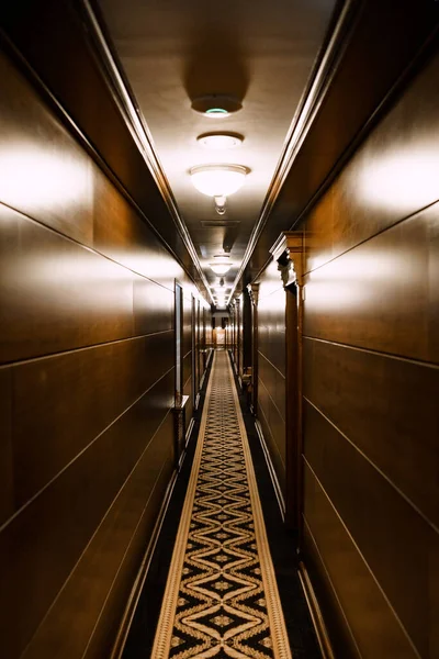 Dark hotel corridor. A long carpet with a pattern, wooden wall cladding. Deserted hotel corridor