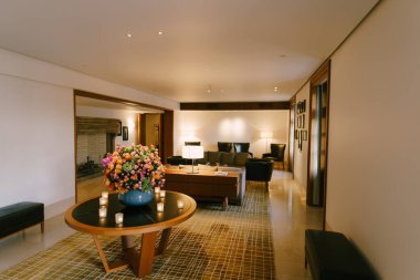 Otel lobisinde. Otelin içi çiçeklerle dolu bir masa, bir kanepe, koltuklar. Ilık ışıklandırma.