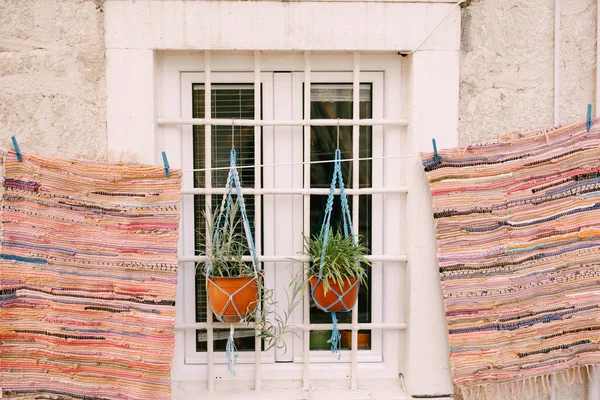 Os tapetes retalhos são secos perto de uma janela branca com uma grade e dois vasos de flores — Fotografia de Stock