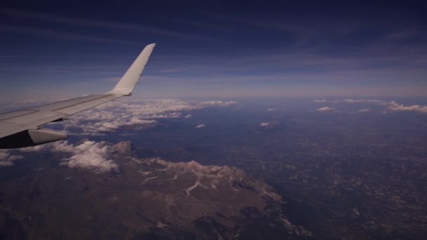 Uitzicht vanaf het vliegtuig naar Gran Sasso en Monti della Laga Nationaal Park in Italië. Luchtfoto van prachtige witte hoop wolken op blauwe lucht. Vleugel van een vliegtuig uit een patrijspoort. Reisconcept — Stockvideo