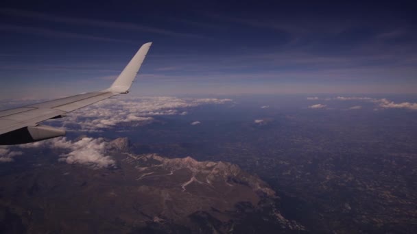 View from the plane to Gran Sasso and Monti della Laga National Park in Italy. Aerial view of beautiful white heap clouds on blue sky. Wing of an airplane from a porthole. Travel concept — Stock Video