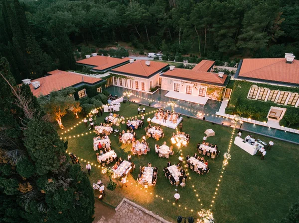 Budva, Montenegro - 10 de junio de 2019: Banquete de bodas, cena, al atardecer a la luz de guirnaldas. Mesas en el banquete y un escenario con un grupo musical en el Aman Resorts Sveti Stefan Spa — Foto de Stock