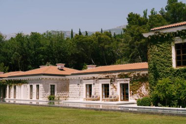 Budva, Karadağ - 10 Haziran 2019: Lüks otel Aman Sveti Stefan. Spa binasının ön cephesi. Sarmaşık dallarıyla kaplı beyaz mermer bina, yerde büyük pencereler, zarif ahşap mobilyalar.
