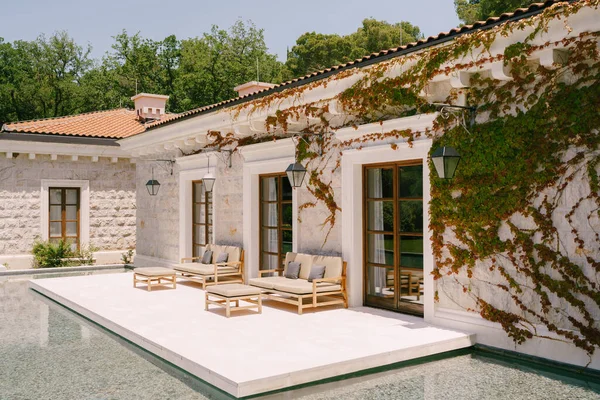 Budva, Montenegro - 10 de junho de 2019: Hotel de luxo Aman Sveti Stefan. A fachada do edifício do spa. Edifício de mármore branco coberto com ramos de hera, grandes janelas no chão, móveis de madeira elegantes — Fotografia de Stock
