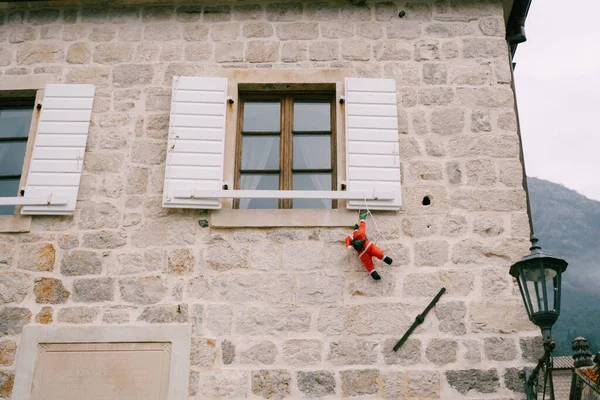Spielzeug-Weihnachtsmann klettert durch ein weißes Fenster mit Rollläden in der Stadt Perast, Montenegro — Stockfoto