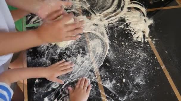 Caring mothers hands knead dough for pies, childrens hands help. Black table and white flour. Children are involved in cooking. Children play with white wheat flour on table. — Stock Video
