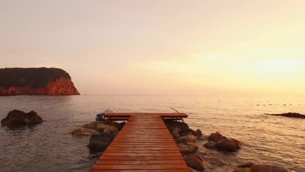Een houten steiger op een zeestrand, de camera vliegt van begin tot eind. Geel gouden zonsondergang boven de zee, vlekken op de hele hemel — Stockvideo