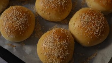 Hamburgerler fırından yeni çıktı, hala sıcak, susam tohumları bol bol serpiştirilmiş. Ev yapımı yuvarlak domuz çörekleri, kırmızı kabuklu.