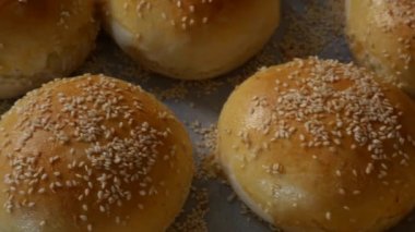 Hamburgerler fırından yeni çıktı, hala sıcak, susam tohumları bol bol serpiştirilmiş. Ev yapımı yuvarlak domuz çörekleri, kırmızı kabuklu.