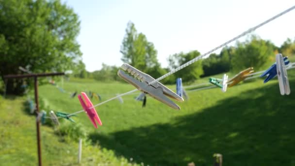 Wäscheklammern an einem weißen Seil, an einem Wäschetrockner, im Wind schwankend vor dem Hintergrund grüner Wiesen und Bäume. — Stockvideo