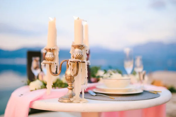 Κοντινό πλάνο ενός τραπεζιού γαμήλιων δείπνων στη δεξίωση. Κάψιμο κεριών σε ένα κηροπήγιο σε ένα τραπέζι με ροζ πανί και πιάτα κρέμας στο φόντο του ουρανού ηλιοβασίλεμα. — Φωτογραφία Αρχείου