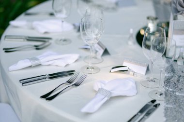 Düğün yemeği masasının yakın çekimi. Çatal bıçak takımı masanın üstünde. Bıçaklar, çatallar, peçeteler peçete için, bardaklar şarap için. Krem masa örtüsü ve çatal bıçak takımı.