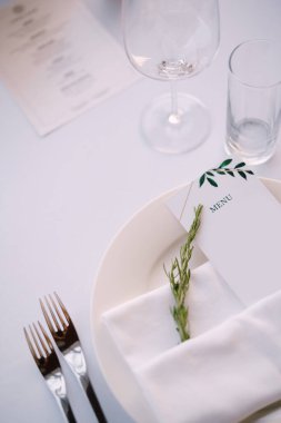 Düğün masası resepsiyonu. Kağıt menü ile bez havlu ve beyaz masa örtüsünün arka planında biberiye filizi
