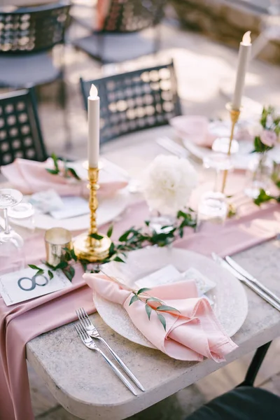 Wedding dinner table reception. Stone table with pink runner, plates with pattern and rag pink napkins, candles with led-light bulbs in the rays of sunset. Top view — Stock Photo, Image