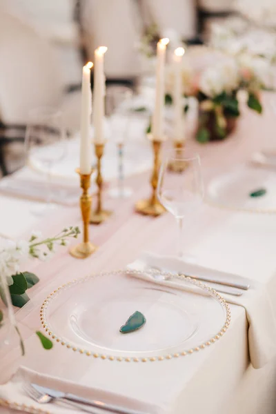 Wedding dinner table reception. Close-up of wildcard with gold beads, transparent glass. Runner of pink silk. Candles in golden candlesticks and flowers in the center of the table. — Stock Photo, Image