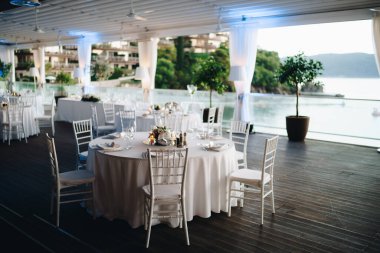 Düğün masası resepsiyonu. Beyaz masa örtüsü ve beyaz Chiavari sandalyeli yuvarlak ziyafet masası. Çadırın altında düğün. 