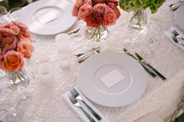 Düğün masası resepsiyonu. Yukardan, beyaz yuvarlak plakalardan yakından bak. Pembe, turuncu, yeşil çiçekler. Pembe güller, küçük turuncu güller. Üst görünüm