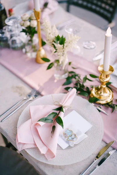 Bröllopsmiddagsbord. Stenbord med rosa löpare, tallrikar med mönster och trasrosa servetter, ljus med LED-lampor i solnedgångens strålar. Ovanifrån — Stockfoto