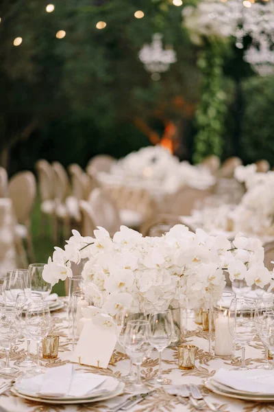 Recepción de mesa de cena de boda. Un gran ramo de orquídeas blancas sobre la mesa entre platos, vasos y velas. Floristería de boda — Foto de Stock